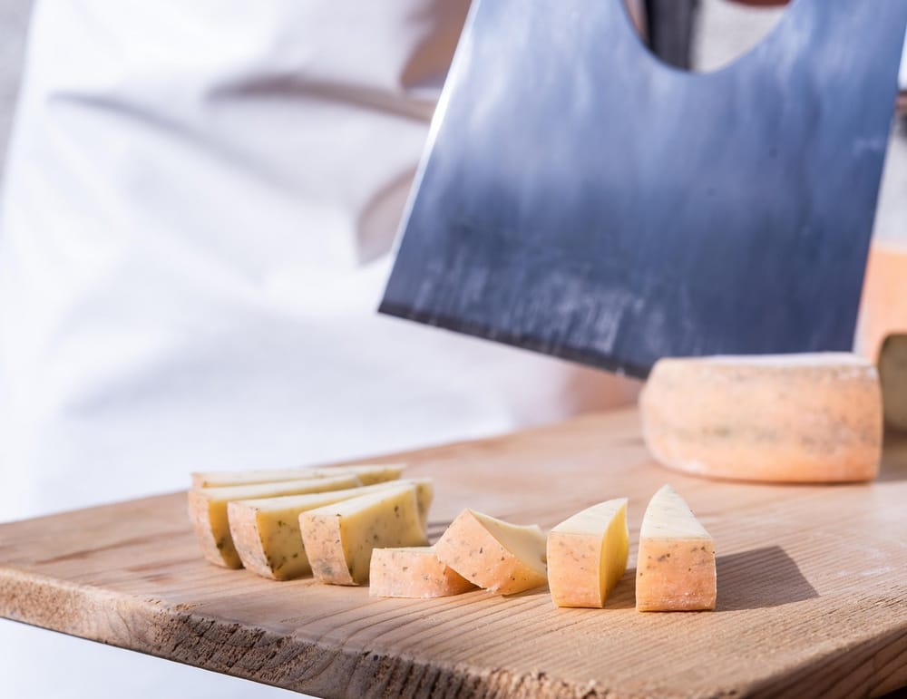 Auf Holzbrett wird Käse vom Senner in kleine Stücke geschnitten