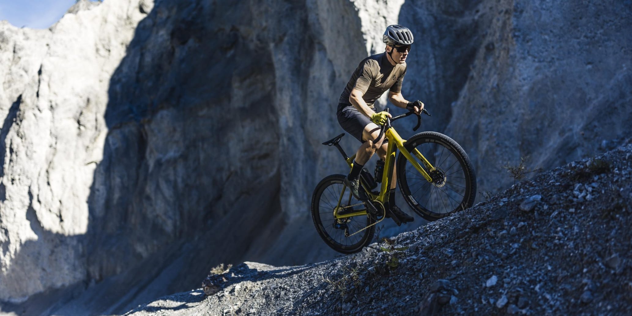 Gravel-Biker auf schmalem Pfad auf losen Steinen unterhalb von einem Felsen