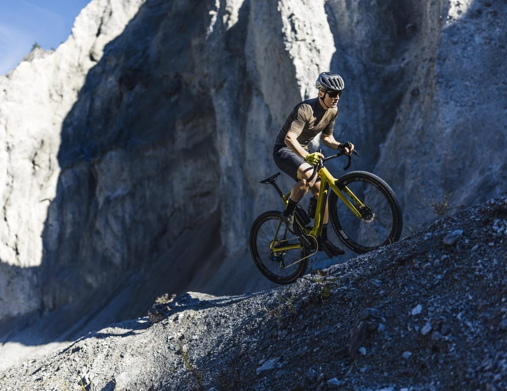 Gravel-Biker auf schmalem Pfad auf losen Steinen unterhalb von einem Felsen