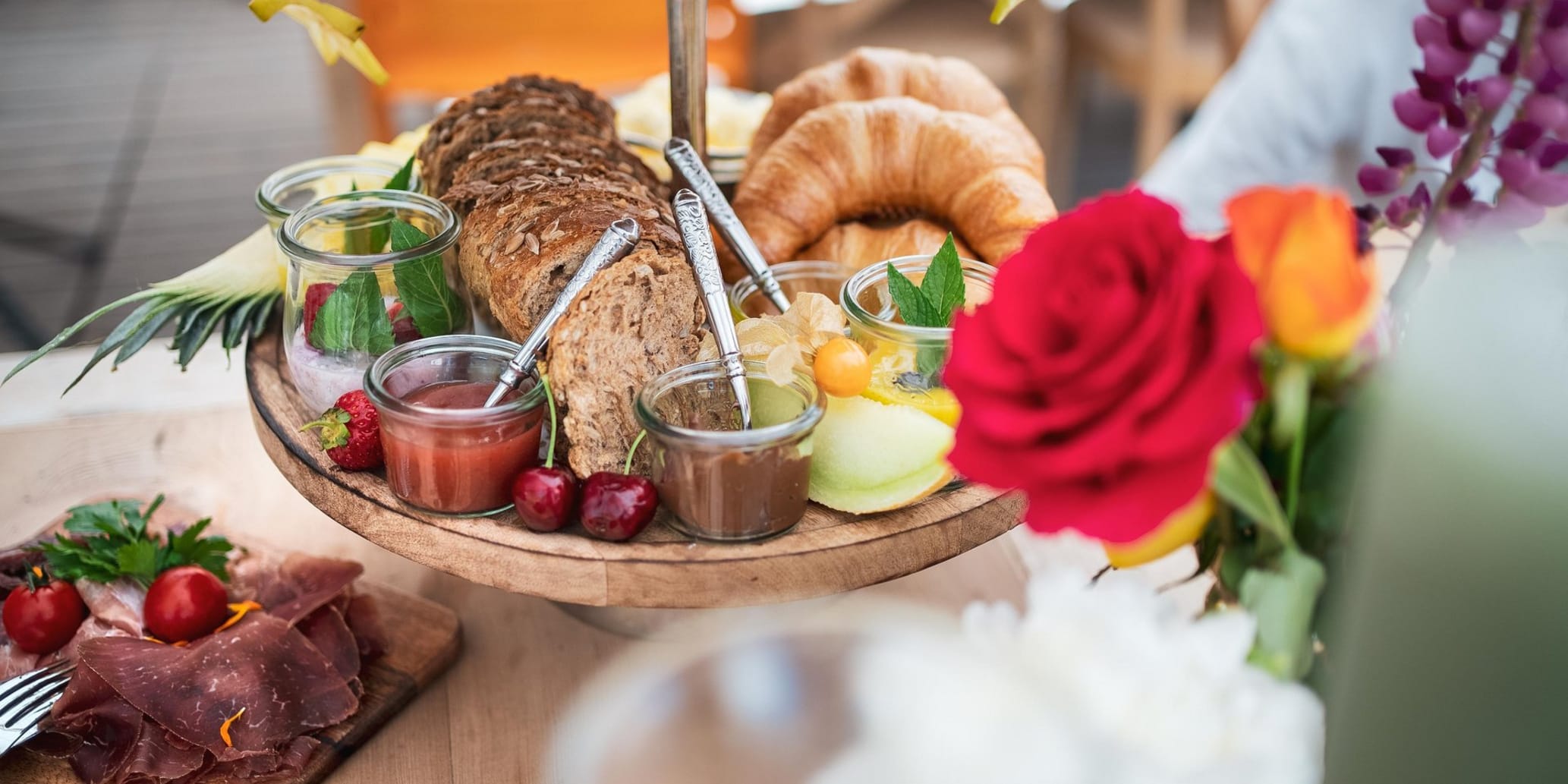Buffet mit Brot, Aufstrich, Fleisch und rechts davon Blumen