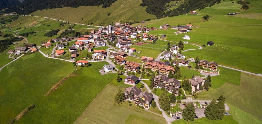 Drohneuaufnahme des Dorfes Lumbrein im Sommer. Wiesen umgeben das Dorf.
